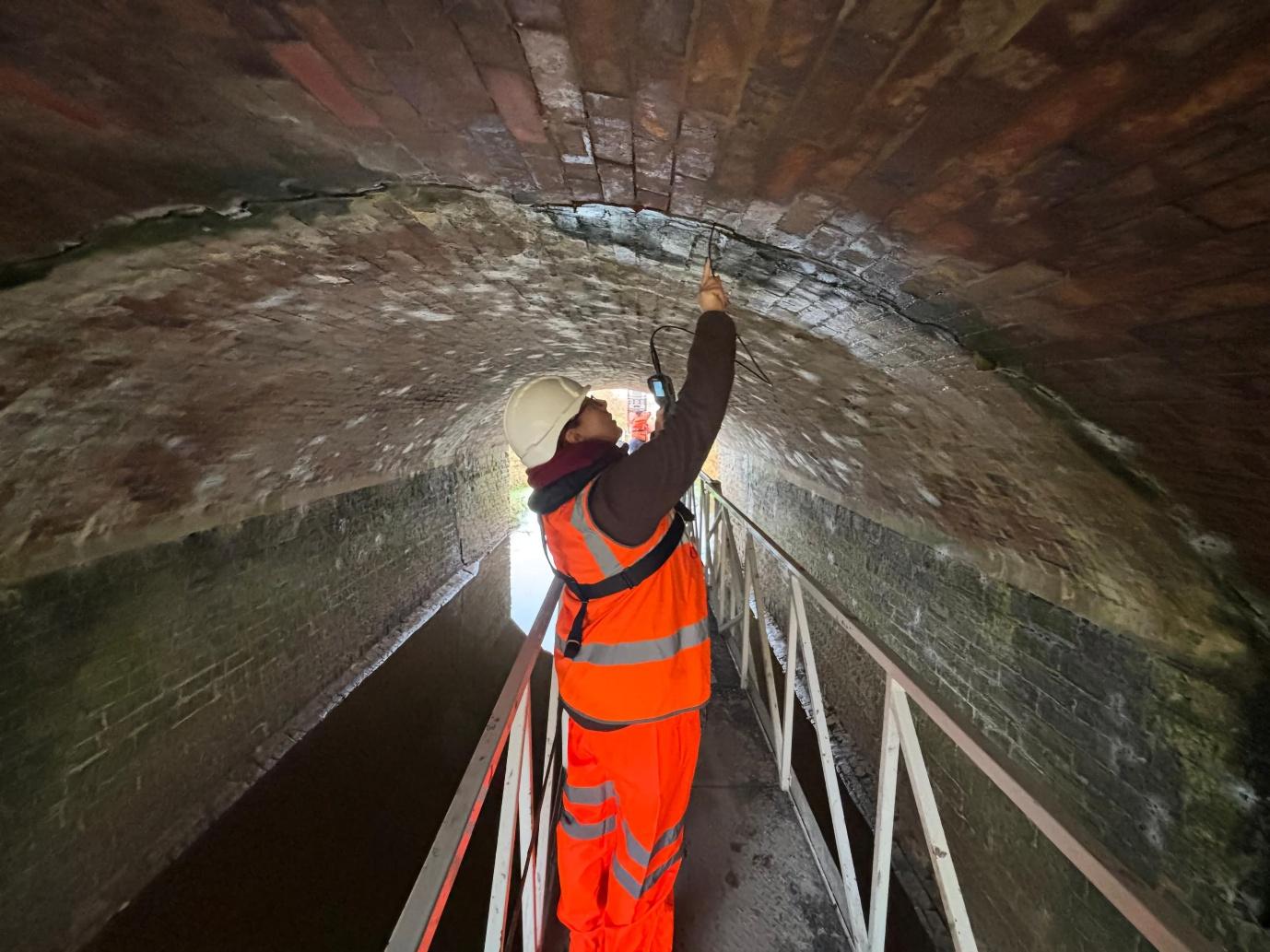 Surveyor inspecting the brickwork beneath a masonry arch while wearing high-visibility PPE.